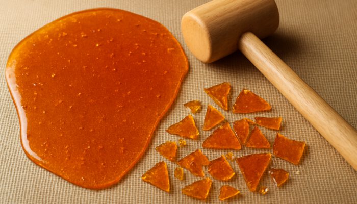Glossy amber praline cooling on silicone mat beside wooden mallet for shattering into shards